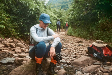 Tired woman hikker resting while trekking with group in wild jungle - 781923935