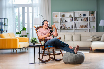 Weekend. Relaxed Indian Man In Wireless Headset Using Mobile Phone Listening To Audiobook Sitting On rocking Chair.