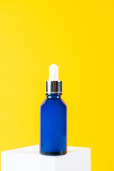 Blue glass cosmetic bottle, Skin care or sunscreen cosmetic with stylish props on yellow background.
