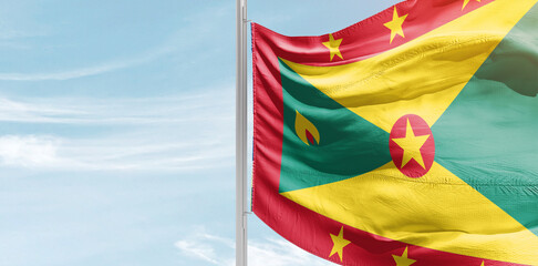 Grenada national flag with mast at light blue sky. - obrazy, fototapety, plakaty