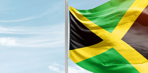 Jamaica national flag with mast at light blue sky.