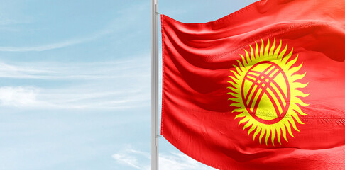 Kyrgyzstan national flag with mast at light blue sky.