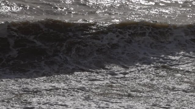 Slow motion shot of dirty water waves rolling and crashing onto cobble beach