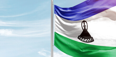 Lesotho national flag with mast at light blue sky.
