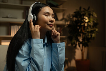 A young woman is immersed in the experience of listening to music through her white over-ear...