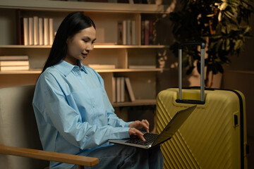 A young Asian woman is engrossed in using her laptop, sitting comfortably by a bright yellow...