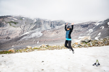Woman tourist jumping on a patch of snow at Skyline Trail. Mt Rainier National Park. Washington State.