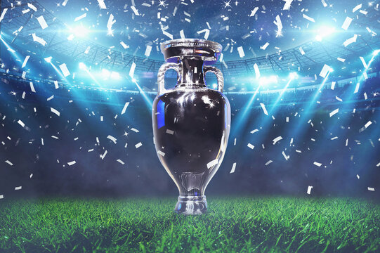 The champion cup stands on a green field at a football stadium with the light of spotlights and confetti. Football cup final, creative idea. Euro 2024 celebration