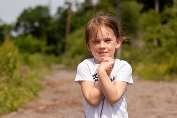 Smiling little cute girl stands on a forest road. Blurred natural background