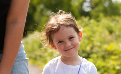 Smiling little cute girl standing in the park next to her mother. Blurred natural background