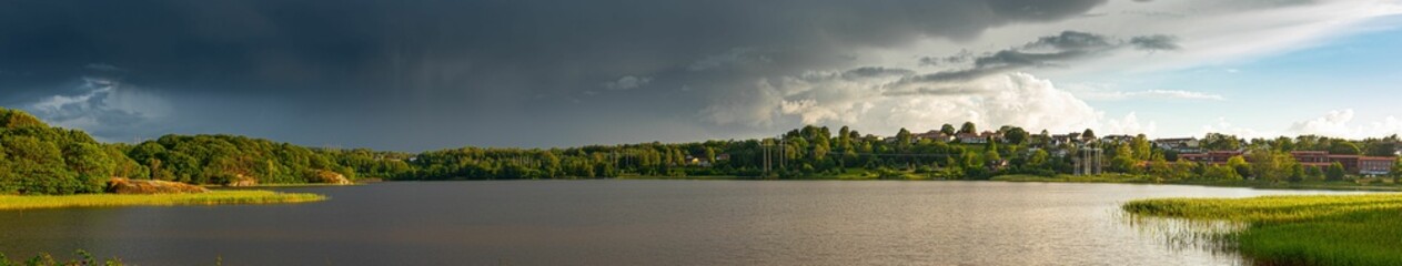 Naklejka na ściany i meble Panoramic view of lake surrounded by green field under cloudy sky