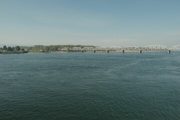Fototapeta premium A steel bridge over the calm Columbia river in Washington, with a forest in the background