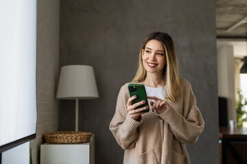 Young woman wearing sweater using smartphone at home, communication and social network concept, - obrazy, fototapety, plakaty