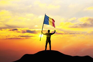 Romania flag being waved by a man celebrating success at the top of a mountain against sunset or sunrise. Romania flag for Independence Day.