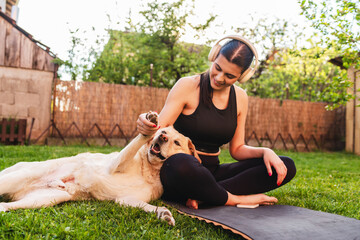 One young caucasian woman is training and doing yoga while playing with her dog outdoors
