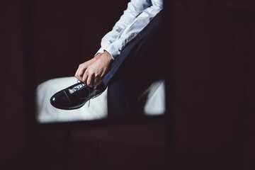 Man sitting on the bed and lacing up his leather shoes on his wedding day - obrazy, fototapety, plakaty