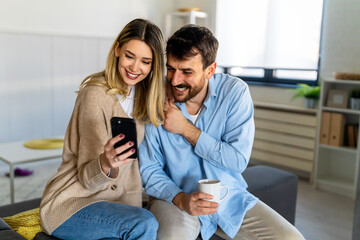 Young happy couple using phone to share social media news at home, doing shopping online. - 781956536