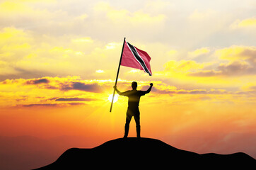 Trinidad and Tobago flag being waved by a man celebrating success at the top of a mountain against...