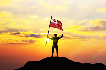 Tonga flag being waved by a man celebrating success at the top of a mountain against sunset or...
