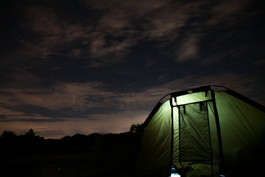 Green tent in an open field at night with a light lit inside
