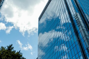 Low angle shot of a modern building with glass facade with the reflection of the cloudy sky