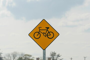 Closeup of a yellow bicycle sign outdoors with clouds in the background