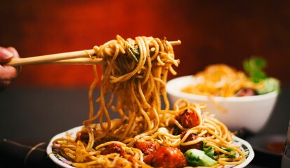 Closeup view of noodles with Manchurian and Schezwan sauce on a chopstick
