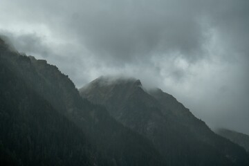 Low angle shot of a mountainside covered in mist in gloomy weather - obrazy, fototapety, plakaty