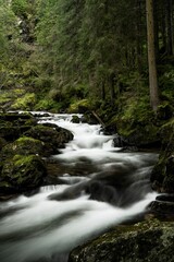 Fototapeta premium Vertical long exposure of waterfall cascades surrounded by evergreen trees