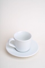 Vertical shot of a white cup of coffee with its plate on a cream surface