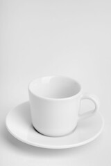 Vertical shot of a white cup of coffee with its plate on a white surface