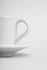 Vertical shot of a white cup of coffee with its plate on a white surface