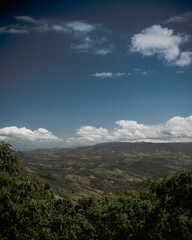 Vertical view of a landscape with mountains and trees against a blue cloudy sky