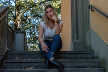 Closeup of a young blonde woman sitting on the stairs and looking at the camera.