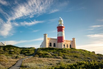 Image of a white and red lighthouse on the top of the mount under the blue sky. - Powered by Adobe