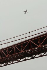 Vertical shot of the Golden Gate Bridge with an airplane flying above in the gray sky
