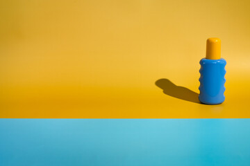 blank sunscreen packaging bottle on minimalist beach of yellow and blue paper in direct sunlight....