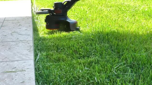 Hand held grass trimmer mowing green lawn. Grass shreds flying around the gardening tool