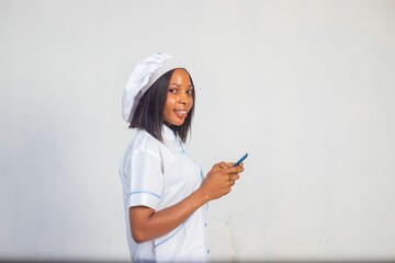 African-American female in a white uniform holding a smartphone and smiling against white background