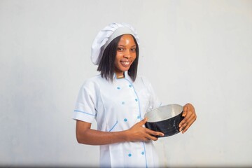 African-American female in a white uniform holding a pot and smiling against a white background