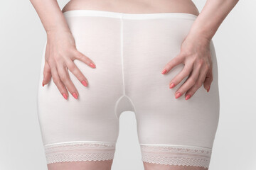 Woman's hips in pantaloons panties, back view of woman with her palms placed on her buttocks. Close-up of the midsection of an unrecognizable plus size female body. Women's health and wellness concept