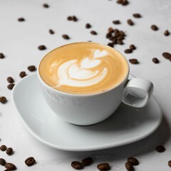 White coffee cup on a white plate surrounded by coffee beans