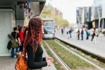 A young red-haired girl waits for the tram, which appears in the background of the image arriving...