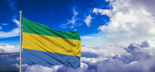 Gabon national flag cloth fabric waving on beautiful Blue Sky Background.
