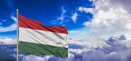 Hungary national flag cloth fabric waving on beautiful Blue Sky Background.