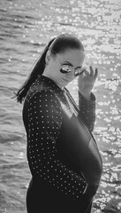 Black and white photo of a pregnant girl with glasses on the background of the sea