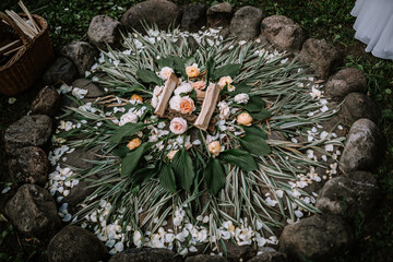 Valmiera, Latvia - July 14, 2023 - A ceremonial Latvian folk floral arrangement on the ground, with white and peach flowers, green leaves, and straw, encircled by rocks.