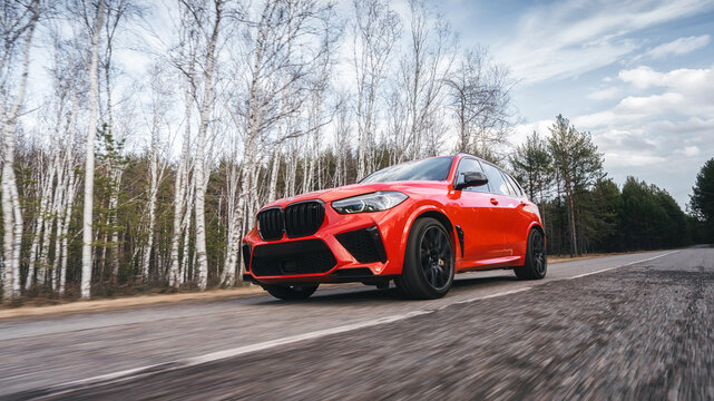 Seattle, Washington, USA April 7, 2024: The red updated BMW X5 m Competition car moves along the highway in the forest. Luxury SUV from a famous German brand. front view