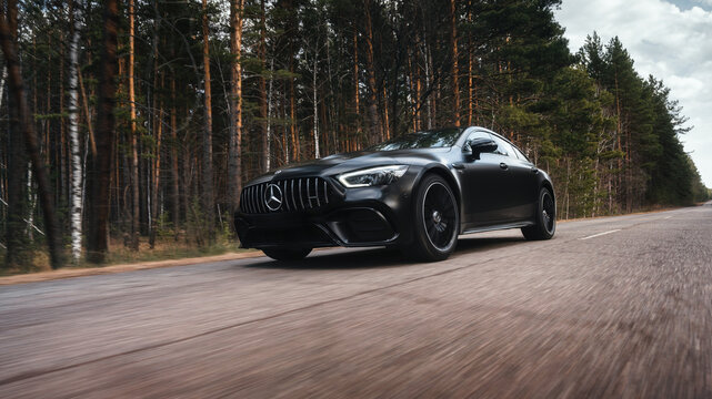 Seattle, Washington, USA April 7, 2024: Mercedes-Benz AMG GT 43 matte black, moving along a highway in the forest. A luxury car from a famous German brand. foreground
