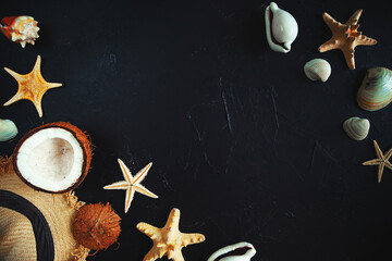 Straw hat, coconut, starfish and seashells on a black background.